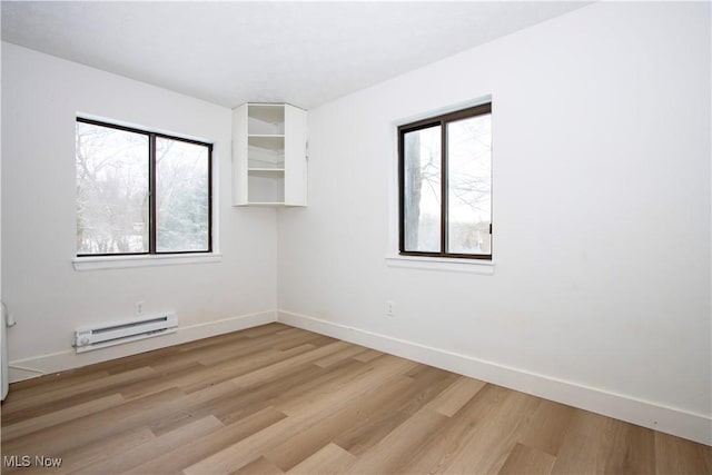 empty room featuring a baseboard heating unit, light hardwood / wood-style flooring, and a healthy amount of sunlight