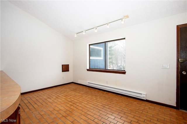 unfurnished room featuring brick floor, track lighting, baseboards, and baseboard heating