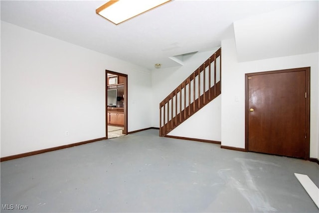 unfurnished room featuring concrete floors, baseboards, and stairs