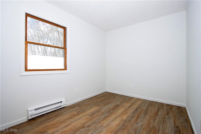 empty room featuring a baseboard heating unit, dark wood-style flooring, and baseboards