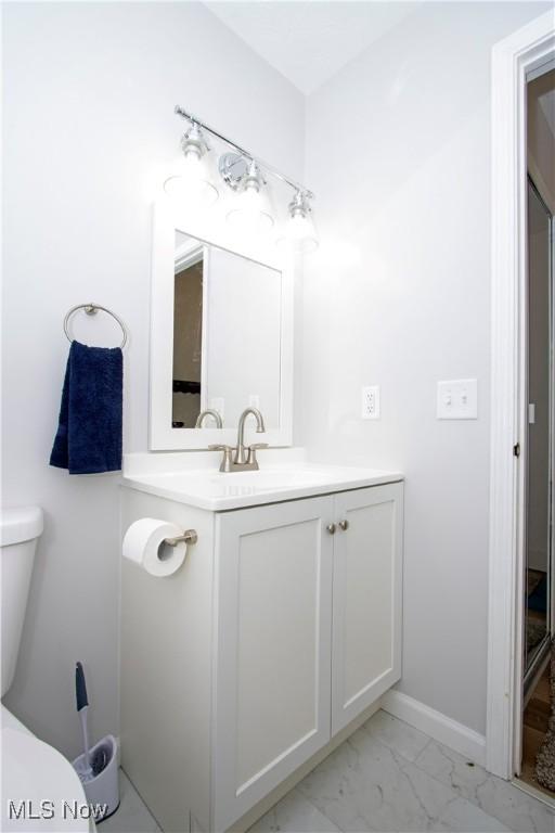 bathroom featuring toilet, marble finish floor, baseboards, and vanity