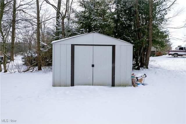 snow covered structure featuring a storage shed and an outbuilding