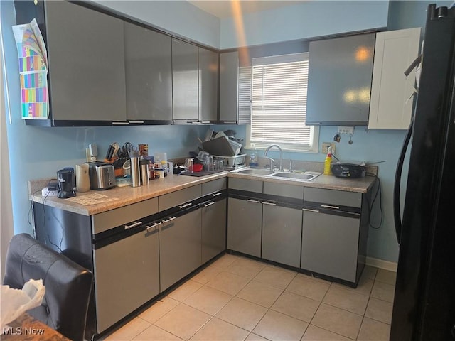 kitchen with black refrigerator, gray cabinets, sink, and light tile patterned floors