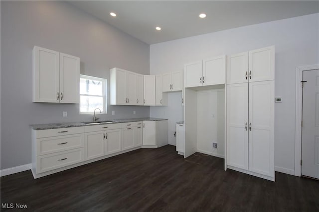 kitchen featuring sink, dark wood-type flooring, a high ceiling, light stone counters, and white cabinets