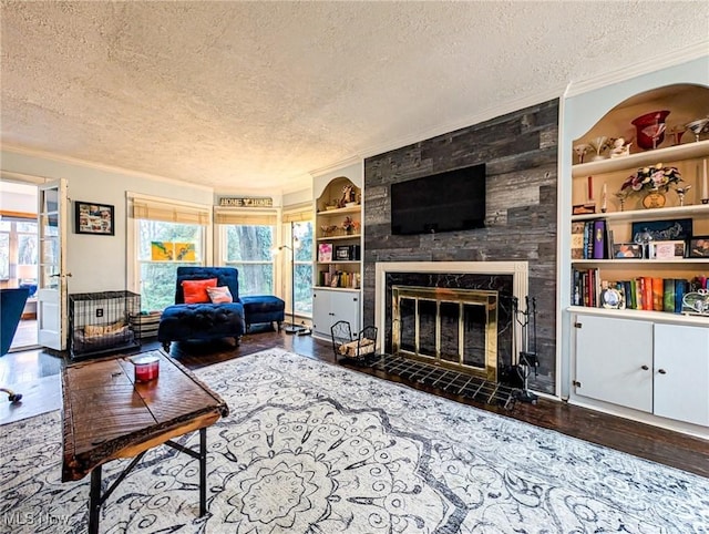 living room with built in shelves, crown molding, a tiled fireplace, and a textured ceiling