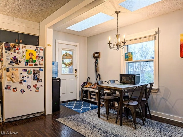 dining area with dark hardwood / wood-style flooring, a textured ceiling, an inviting chandelier, and a skylight