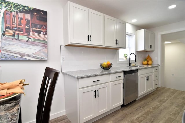 kitchen with light wood-type flooring, decorative backsplash, stainless steel dishwasher, white cabinets, and a sink