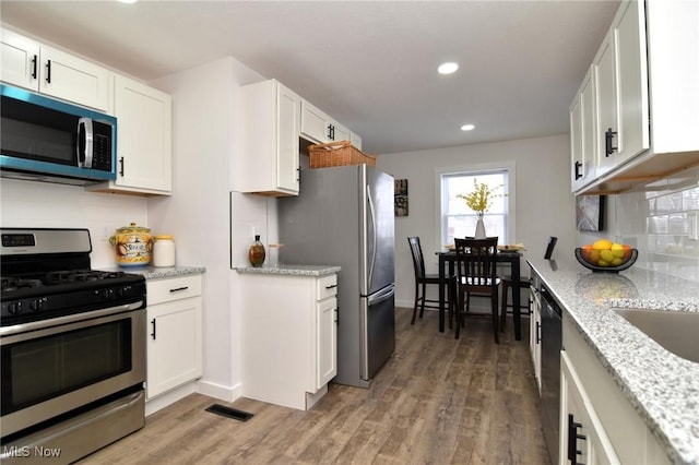 kitchen with visible vents, backsplash, light wood-style flooring, appliances with stainless steel finishes, and white cabinets