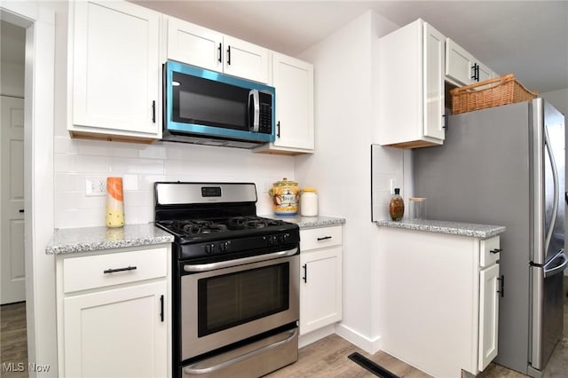 kitchen with decorative backsplash, white cabinets, and appliances with stainless steel finishes