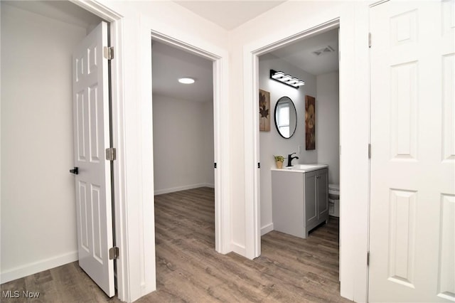 hall featuring a sink, visible vents, baseboards, and wood finished floors