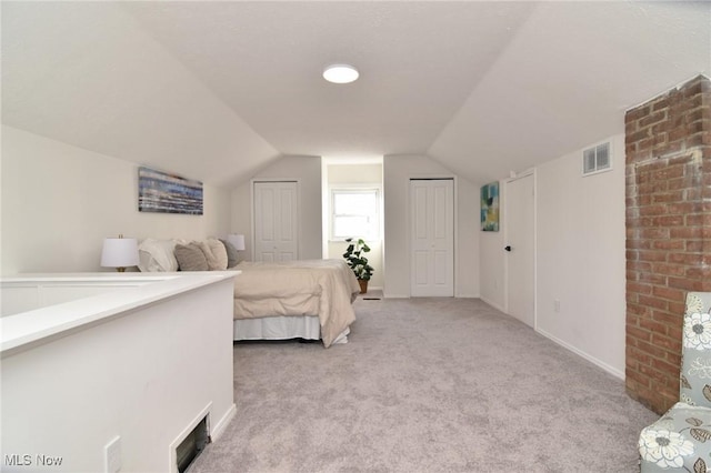 carpeted bedroom with visible vents, two closets, and vaulted ceiling