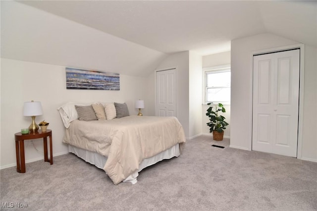 bedroom with vaulted ceiling, light colored carpet, baseboards, and two closets