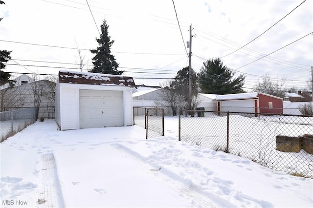 snowy yard with a garage, an outbuilding, and fence