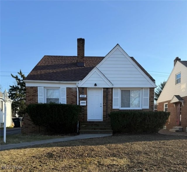 view of front of house featuring brick siding, entry steps, a chimney, and roof with shingles