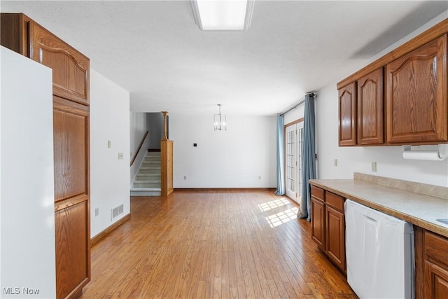 kitchen with white dishwasher, light hardwood / wood-style floors, hanging light fixtures, and a notable chandelier