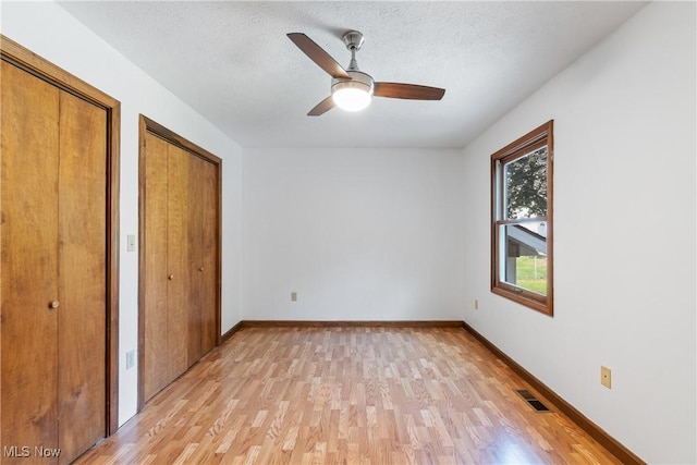 unfurnished bedroom with two closets, a textured ceiling, ceiling fan, and light wood-type flooring