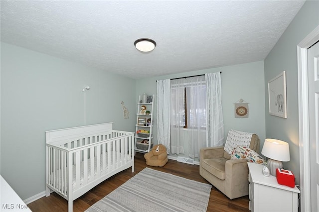 bedroom featuring dark hardwood / wood-style flooring, a textured ceiling, and a crib