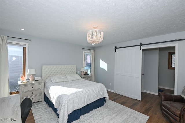 bedroom with a barn door, dark wood-type flooring, an inviting chandelier, and a textured ceiling