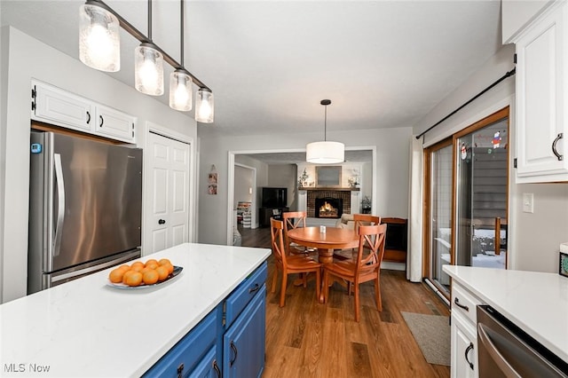 kitchen with pendant lighting, stainless steel appliances, a fireplace, white cabinets, and blue cabinets