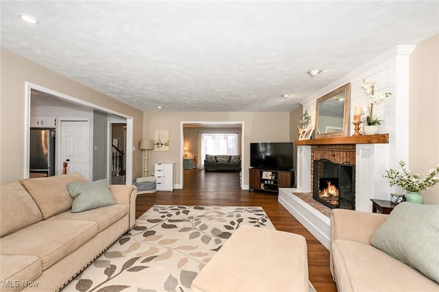 living room with a brick fireplace and dark wood-type flooring