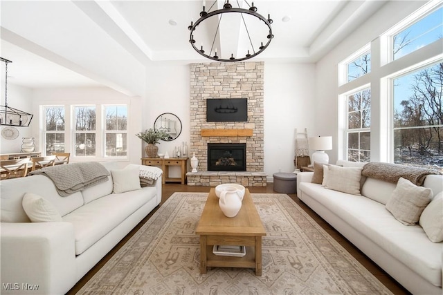 living room with a healthy amount of sunlight, a stone fireplace, light wood-type flooring, and a notable chandelier