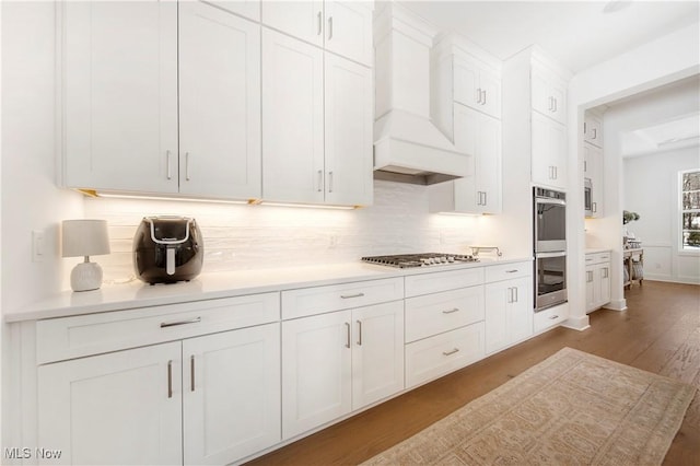 kitchen featuring premium range hood, white cabinetry, stainless steel appliances, light hardwood / wood-style floors, and decorative backsplash