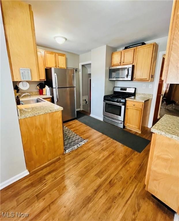 kitchen with stainless steel appliances, wood-type flooring, light stone countertops, and sink