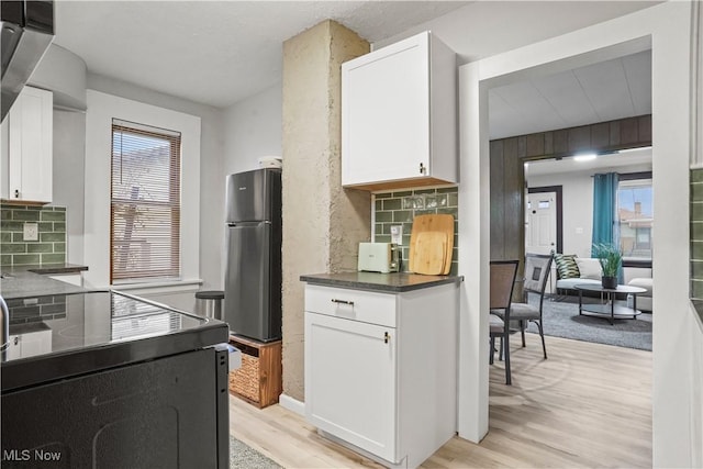 kitchen with white cabinetry, backsplash, stainless steel fridge, and a wealth of natural light