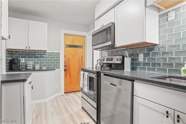 kitchen with light wood-type flooring, appliances with stainless steel finishes, white cabinets, dark stone counters, and backsplash