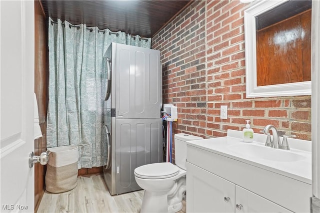 bathroom with stacked washing maching and dryer, brick wall, wood-type flooring, and vanity