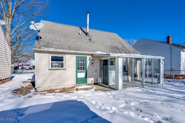 snow covered back of property featuring a sunroom