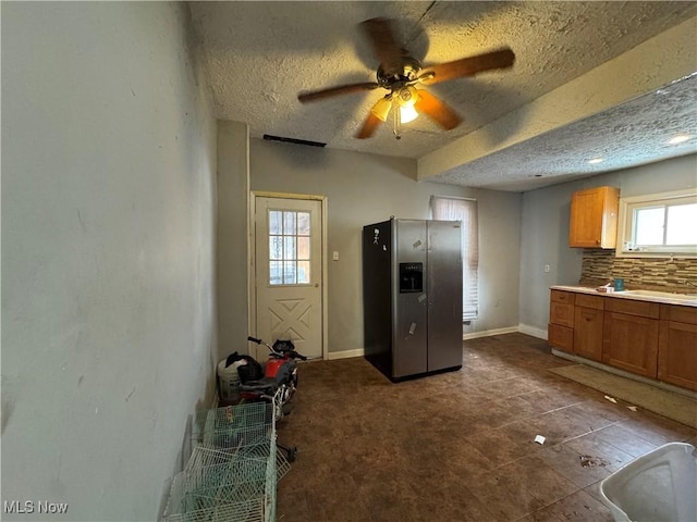 kitchen with decorative backsplash, a wealth of natural light, a textured ceiling, and stainless steel refrigerator with ice dispenser