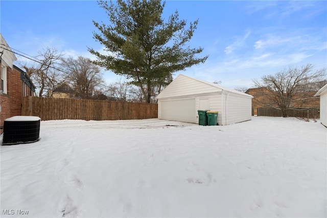 yard covered in snow featuring a garage, an outbuilding, and central air condition unit