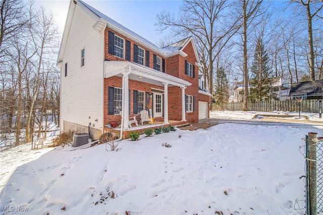 view of snowy exterior with cooling unit, a garage, and covered porch