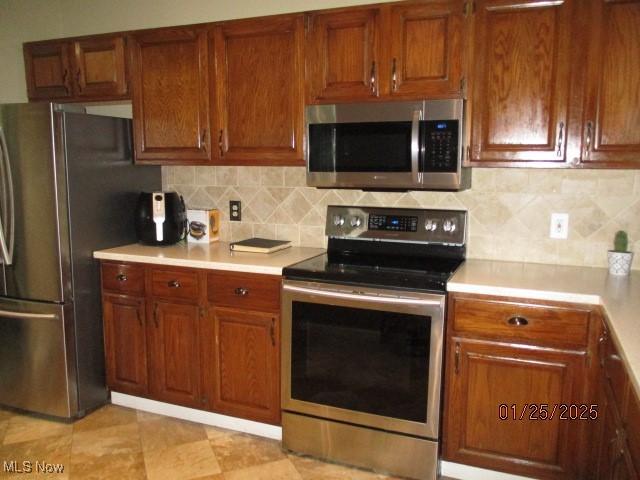 kitchen featuring stainless steel appliances, light tile patterned floors, and backsplash