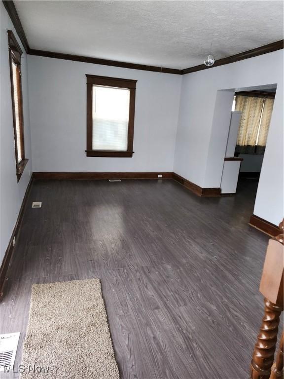 empty room featuring dark wood-type flooring, ornamental molding, and a textured ceiling