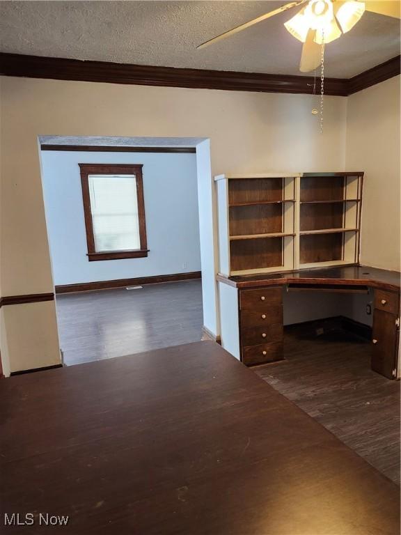 unfurnished office with ornamental molding, dark wood-type flooring, built in desk, and a textured ceiling