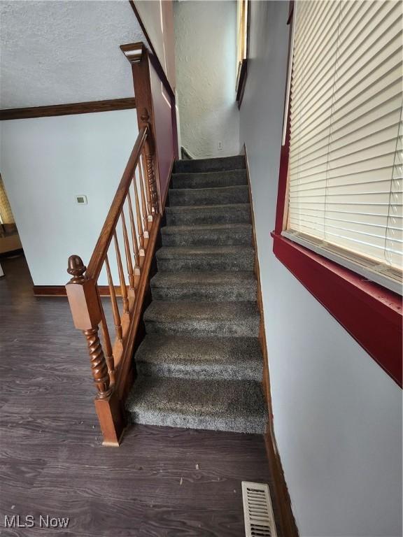 stairway with hardwood / wood-style flooring, ornamental molding, and a textured ceiling