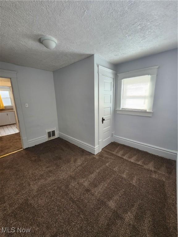 unfurnished room featuring dark carpet, a textured ceiling, and a wealth of natural light