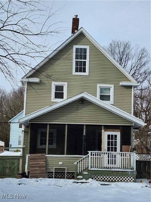 snow covered back of property with a sunroom