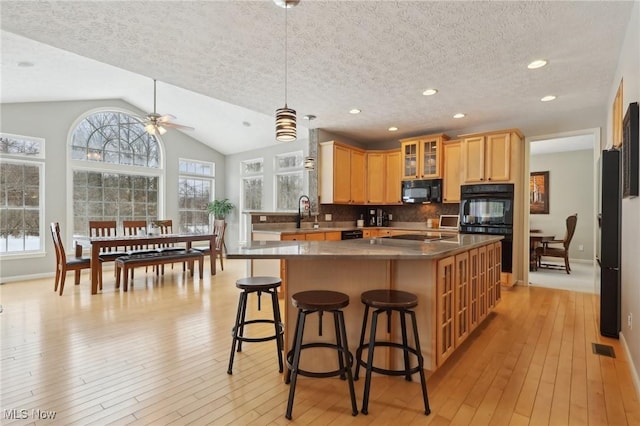 kitchen with backsplash, black appliances, a textured ceiling, a kitchen island, and vaulted ceiling