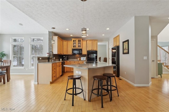 kitchen featuring a textured ceiling, hanging light fixtures, a kitchen island, and black appliances