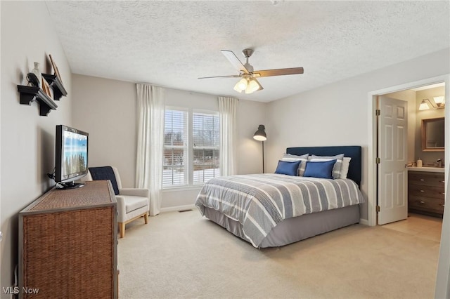 bedroom with ensuite bath, light colored carpet, ceiling fan, and a textured ceiling