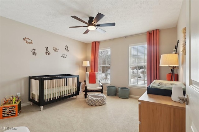 bedroom with a nursery area, a textured ceiling, carpet, and ceiling fan