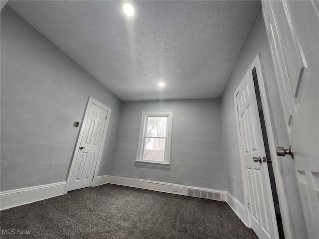 unfurnished room featuring dark colored carpet and a textured ceiling