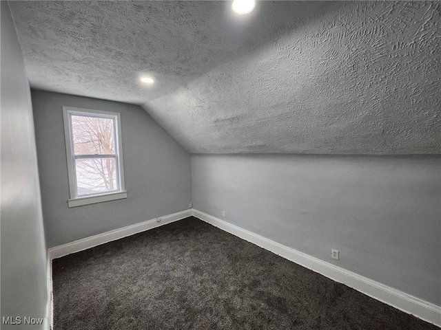 additional living space featuring vaulted ceiling, a textured ceiling, and dark colored carpet