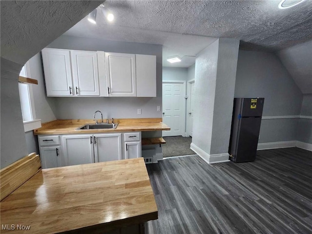 kitchen with wood counters, sink, black fridge, white cabinetry, and a textured ceiling