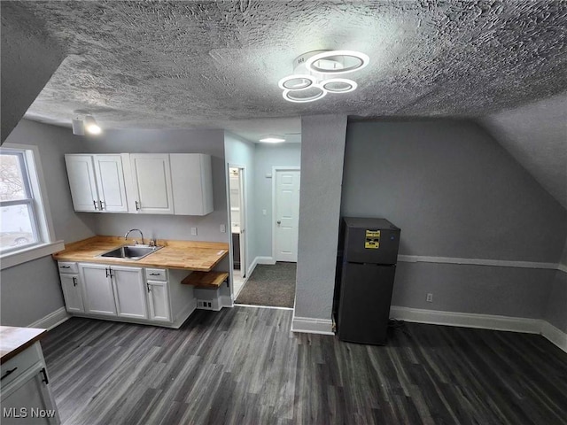 kitchen featuring butcher block countertops, sink, white cabinets, dark hardwood / wood-style flooring, and black fridge