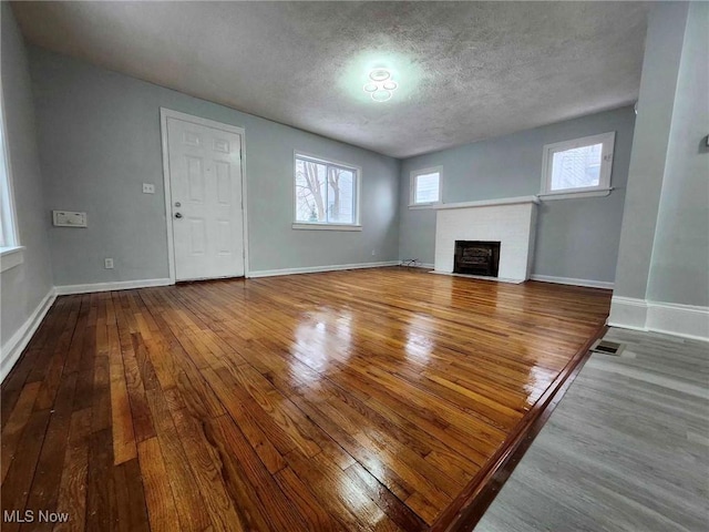 unfurnished living room with hardwood / wood-style floors, a textured ceiling, and a brick fireplace