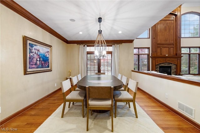 dining space with ornamental molding, plenty of natural light, a stone fireplace, and light wood-type flooring